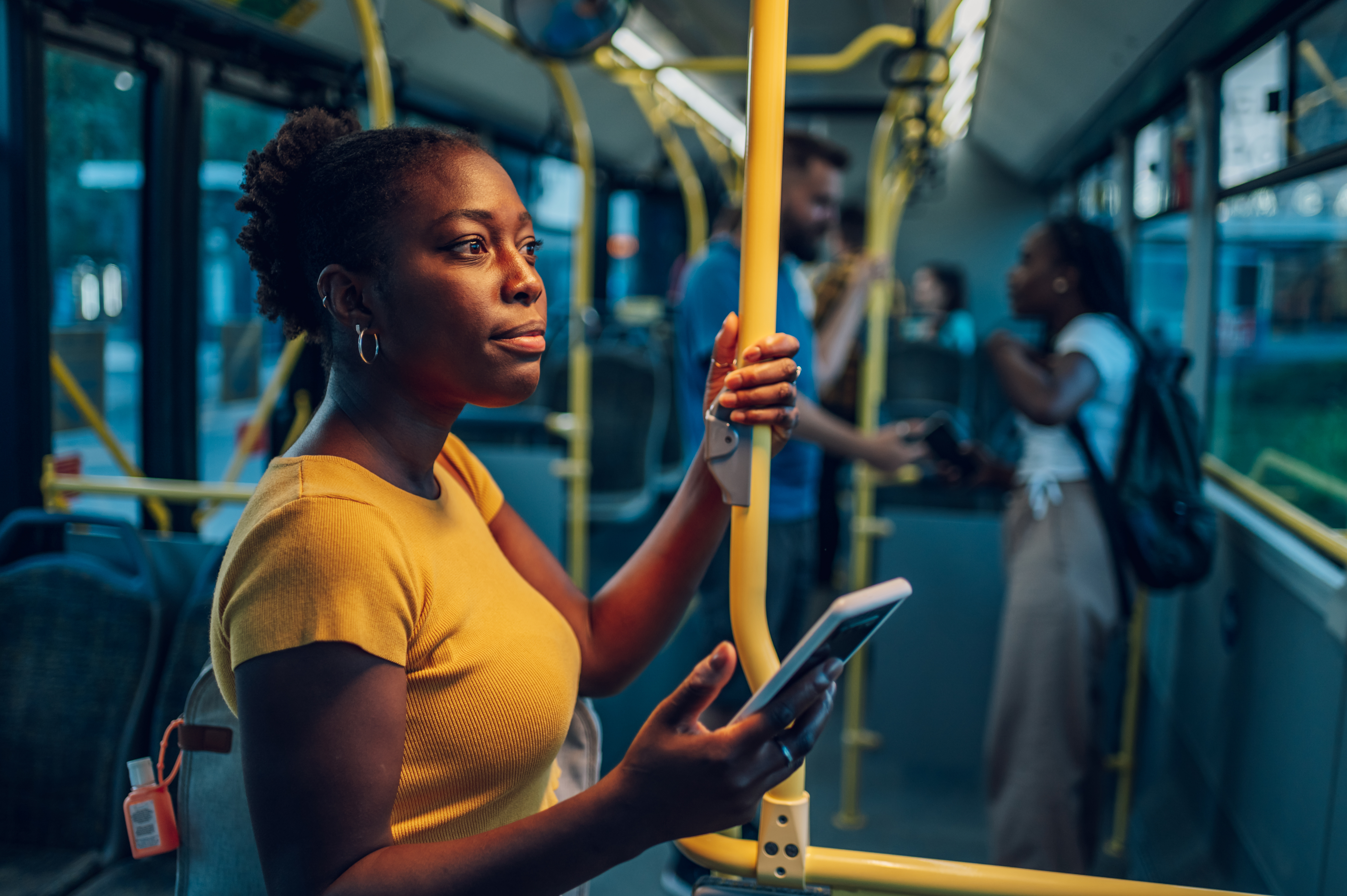 Woman in a yellow shirt and holding her cell phone while alertly standing in a bus.